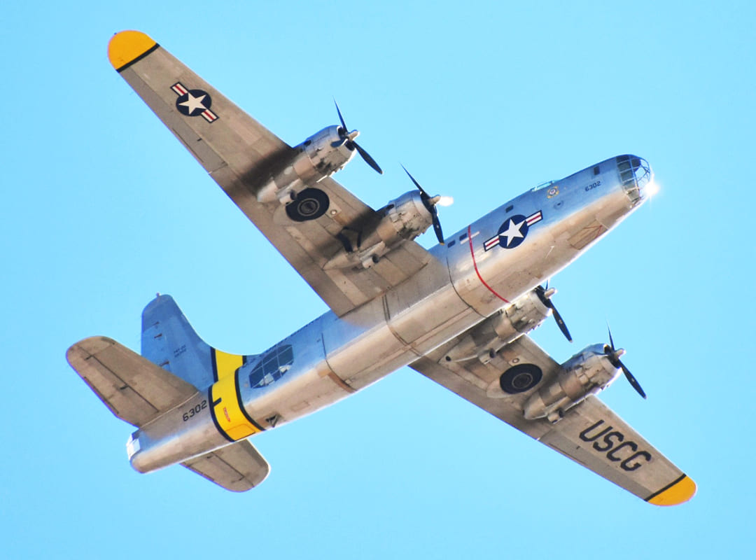 A P4Y-2G Privateer aircraft flies overhead, against a clear blue sky.