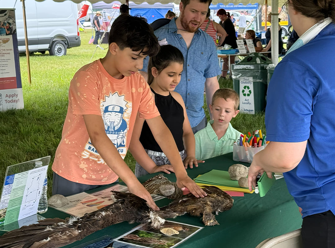 Children examine preserved bird specimens and natural artifacts while participating in an interactive wildlife education activity at the Exploration Station during Thunder Over Michigan.