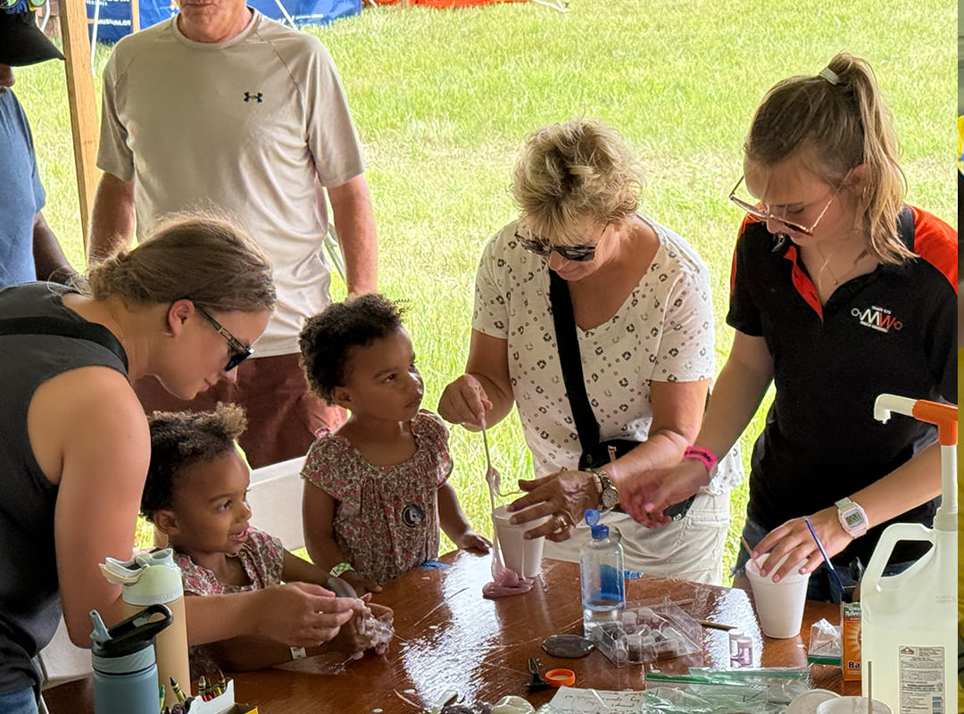 Children and adults participate in a hands-on science activity, mixing materials and observing results with guidance from a volunteer at the Hands On Hangar during Thunder Over Michigan.