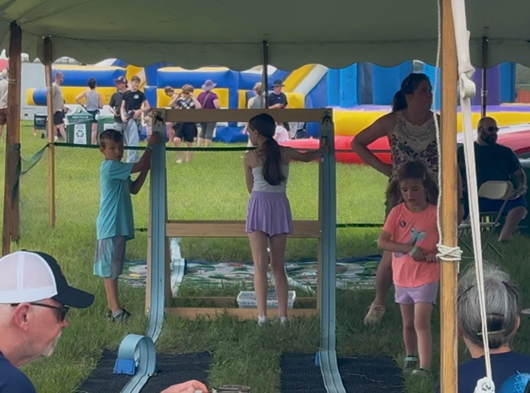 Children interact with a large educational exhibit while families observe nearby inside the Hands On Hangar, with Adventure Zone attractions visible in the background.