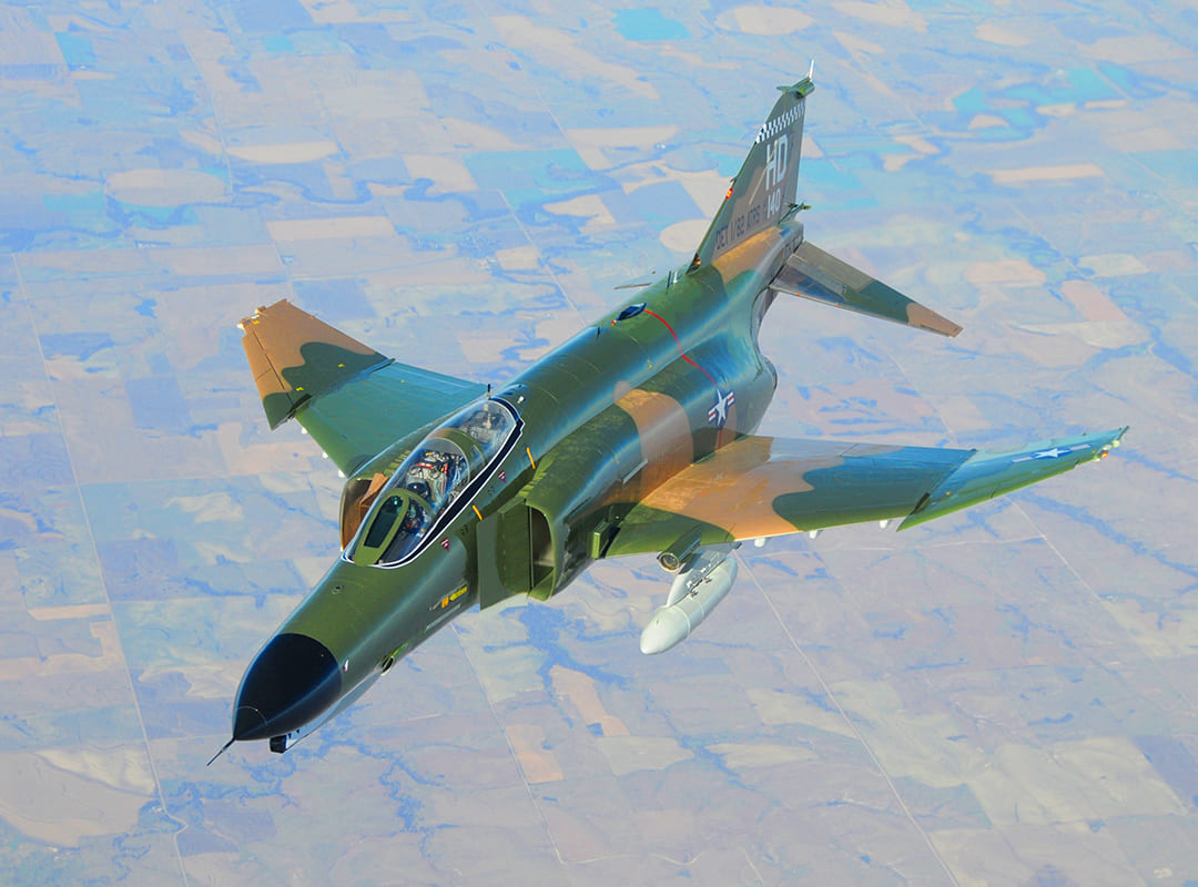 An F-4 Phantom II flies over a rural area.